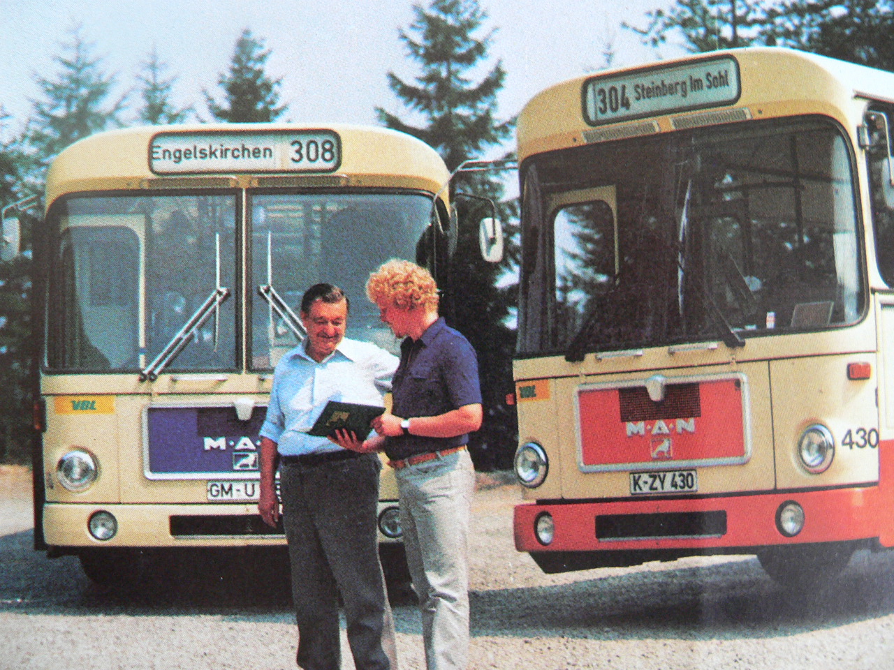 Auf dem Bild sind zwei Busse der Firma MAN sowie zwei Mitarbeiter, die sich unterhalten, zu sehen